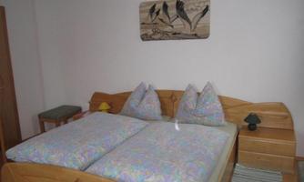 A cozy bedroom with a double bed and colorful pillows. There is also a nightstand and a wooden sculpture on the wall.