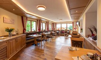 A cozy restaurant area with wooden furniture and several windows. The room is well-lit and friendly designed.