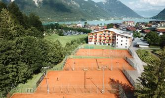 A beautiful complex with several tennis courts and a lovely hotel nearby. In the background, mountains and a lake are visible.