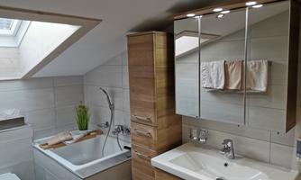 A modern bathroom with wooden furniture and bright tiles. There is a bathtub, a sink, and natural light from the skylight.