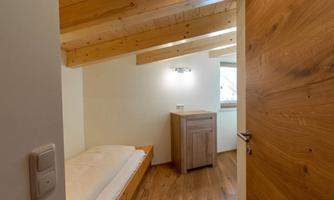 A simple bedroom with wooden details and a window. There is a bed and a small wardrobe.