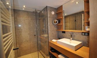 A modern bathroom with a glass shower and elegant stone masonry. A white sink sits on a wooden shelf, and there are soft towels in sight.