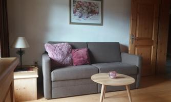 A cozy living room with a gray sofa and a small round table. On the wall hangs a picture of flowers, and there is a lamp on the table.