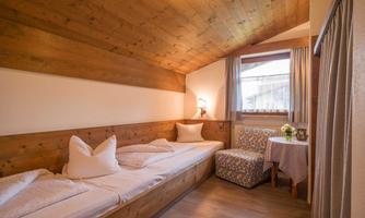 A cozy room with wooden paneling and two single beds. The light is warm and a small table with flowers is by the window.