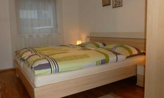 A cozy bedroom with a large bed and colorful bedspreads. Two pictures hang on the wall, and there is a small rug on the floor.