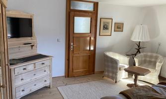 A cozy room with wooden furniture and a television. There are two armchairs and a table, as well as access to the door.