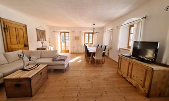 A cozy living room with wooden floors and large windows. There is a bright sofa, a wooden table, and a television.