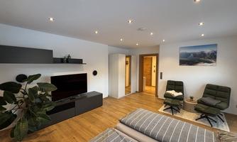 A modern bedroom with a large bed and stylish chairs. The walls are painted light, and there is a cozy atmosphere.