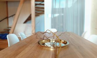 A modern wooden dining table with a round golden plate in the middle. In the background, there are stairs and curtains.