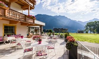 An inviting terrace with white furniture and colorful flowers. In the background, the mountains and a clear sky can be seen.