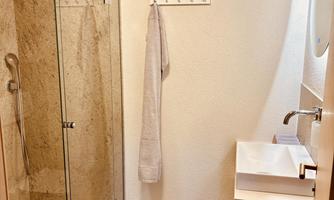A modern bathroom with a large glass shower, stone, and a white sink. The walls are light and the floor looks elegant.