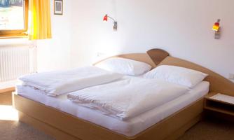 A cozy bedroom with a double bed and white bedspreads. It has large windows with a view outside and simple, modern furnishings.