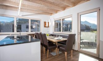 A modern dining area with a wooden table and chairs. Large windows provide a view of the mountains and plenty of daylight.