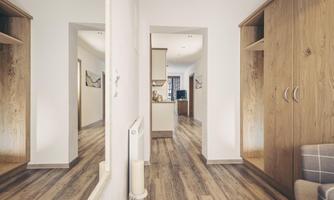 A bright hallway with wooden floors and large cabinets. In the background, a modern kitchen is visible.