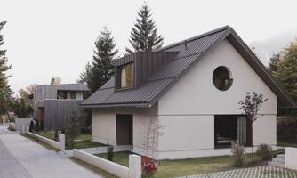 A modern house with a sloping roof and round windows. Surrounded by trees and a well-maintained garden.