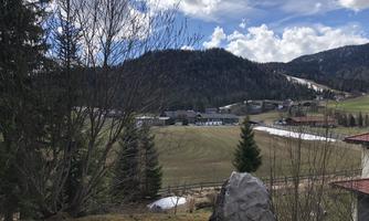 A picturesque landscape with gentle hills and wooded mountains. In the foreground, there is a large stone and some trees.