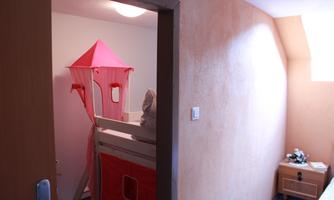 A children's room with a loft bed in the shape of a castle and a small nightstand. The walls are painted in soft colors and there is plenty of daylight.