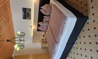 A cozy bedroom with a large bed and checked pillows. The walls are light, and there is a wooden ceiling as well as a beautiful chandelier.