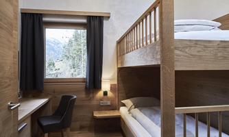 A cozy bedroom with a bunk bed and a window overlooking a forest landscape. The furnishings are made of light wood and provide a pleasant, calm atmosphere.