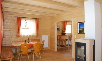 A cozy, brightly decorated room with wood paneling. There is a dining area with a table and chairs as well as a modern kitchen corner.