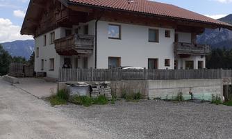 A cozy house with a red roof and several balconies. The surrounding area is filled with nature and a gravel path.