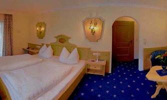 A cozy hotel room with two separate beds and traditional wooden paneling. The room is bright and friendly decorated with a blue carpet and a small seating area.