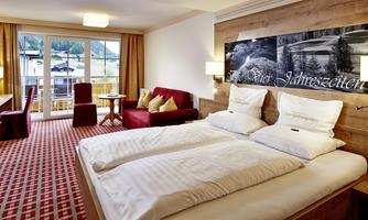 A modern hotel room with a double bed and red accents. Large windows provide views of the surroundings and plenty of natural light.