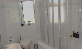 A modern bathroom with a bathtub and shower cubicle. Bright tiles and a window create a friendly atmosphere.