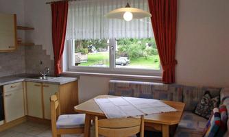 A cozy kitchen with a dining table and seating. Outside the window, you can see a green garden.