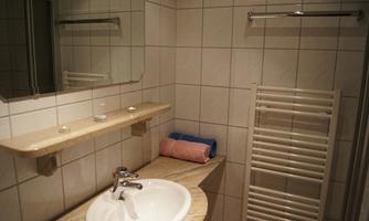 A modern bathroom with a sink and a mirror. On the countertop are two towels and a towel warmer is visible.