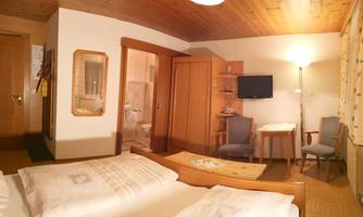 A cozy room with two beds, a table and chairs. There is a television and a door to the bathroom.
