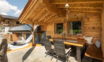 A cozy wooden house with a covered terrace. On the terrace, there are garden furniture and a hammock for outdoor relaxation.