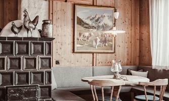 A cozy room with wooden paneling and a seating area. A painting of mountains and cows hangs on the wall.