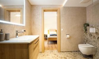 A modern bathroom with a bright, minimalist design. A bedroom is visible through the door.