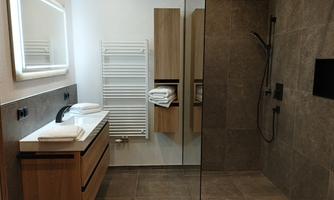 A modern bathroom with a large shower and elegant tiles. It includes wooden cabinets and fresh towels on the shelf.