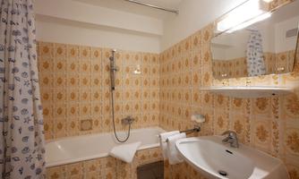 A bathroom with a bathtub and a shower. The walls are decorated with yellow tiles featuring a floral pattern.