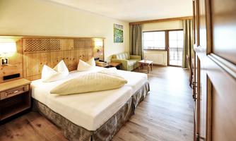 A modern hotel room with a large bed and wooden details. The windows provide plenty of natural light and a view of the surroundings.