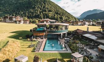 A modern hotel with a pool amidst a picturesque mountain landscape. The surroundings are green and inviting, perfect for a relaxing stay.