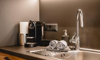 A modern kitchen corner with an elegant faucet, a coffee machine, and towels. The space is stylishly illuminated and has a minimalist atmosphere.