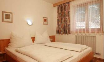 A cozy bedroom with a double bed and large pillows. The room has soft curtains and warm lighting.