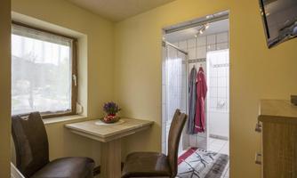 A bright bathroom with a shower and a small table with chairs. On the table, there is a flower vase, and bathrobes are visible in the background.