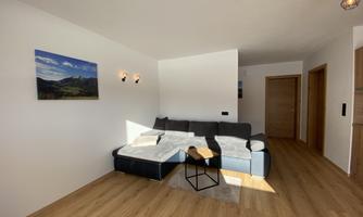 A modern living room with a comfortable sofa and hardwood floor. A landscape picture hangs on the wall, and there is warm lighting.