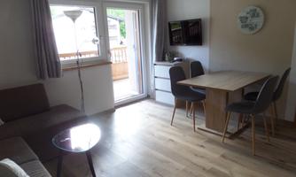 A bright living room with a cozy sofa and a dining table. Large windows let in plenty of daylight.
