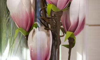An elegant floral decoration featuring pink and white artificial magnolias. The flowers are arranged in a transparent container.