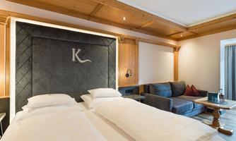 A modern hotel room with two twin beds and a cozy sofa. The wooden walls give the room a warm atmosphere.