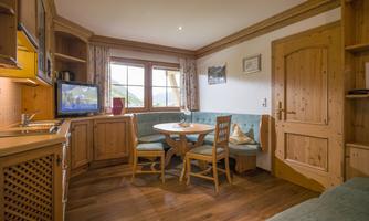 A cozy living space with a dining area and a kitchenette. Large windows provide plenty of daylight and a pleasant atmosphere.