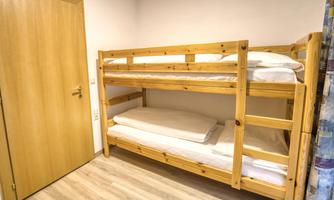 A simple room with a double-decker wooden loft bed. The room has a wooden floor and a wooden door.