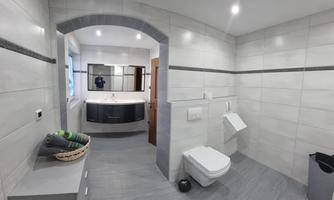 A modern bathroom with gray tiles and an elegant bathtub. There is a large mirror and plenty of space for a tranquil atmosphere.