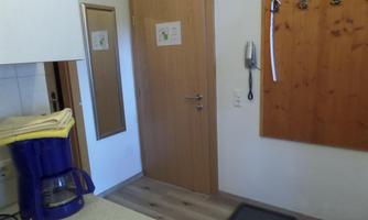 A small kitchenette with a coffee machine and a mirror. Hooks hang on the wall and a door leads outside.