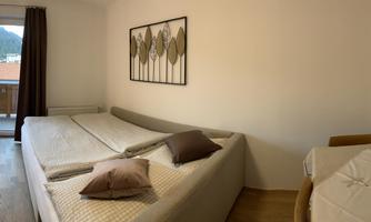 A modern, bright room with two beds and a cozy armchair. The windows offer a view of the landscape.